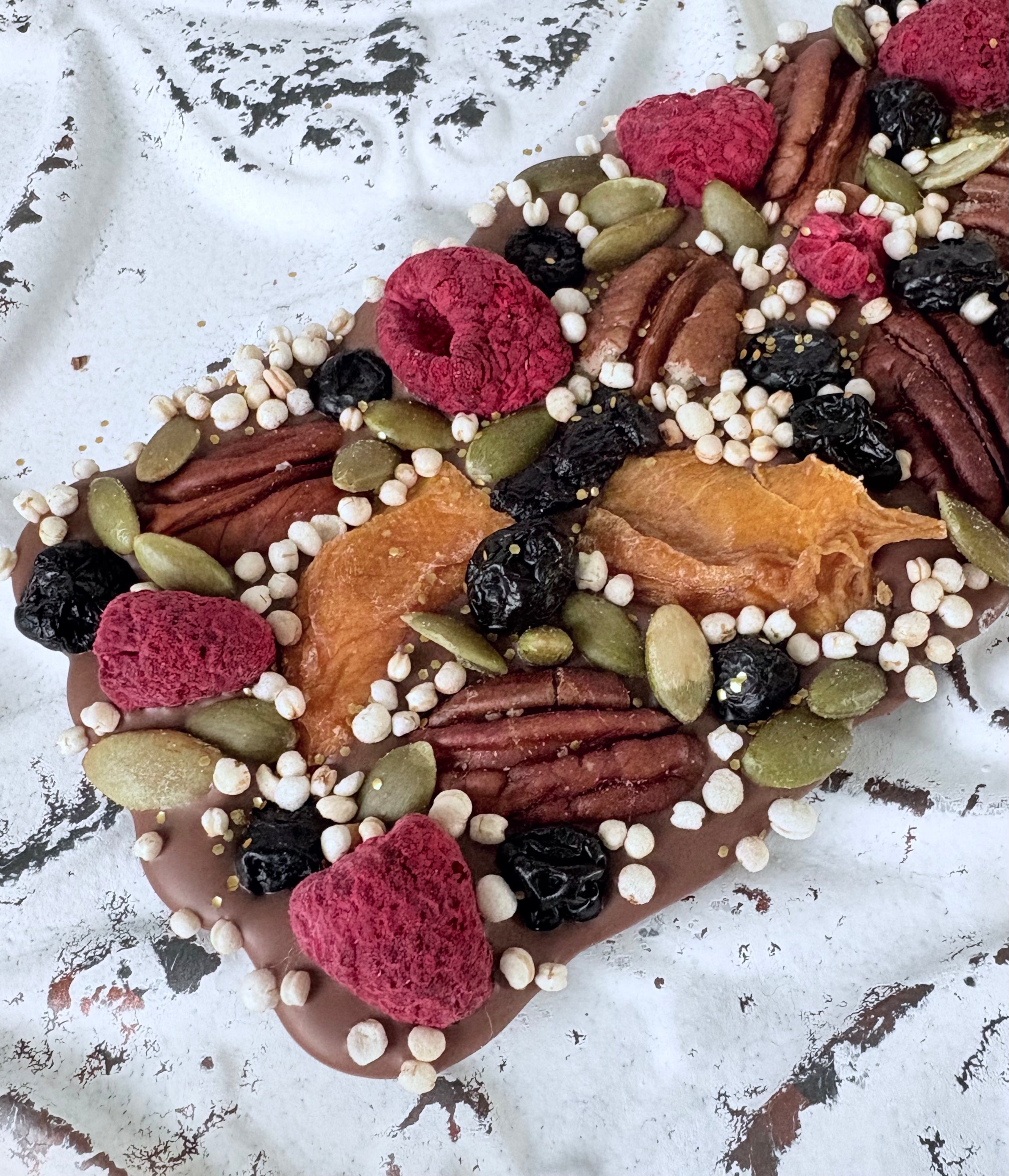 Belgian chocolate bark with freeze-dried raspberries, dried blueberries, full pecans, dried mango, pepitas and puffed quinoa, finished with gold accents.